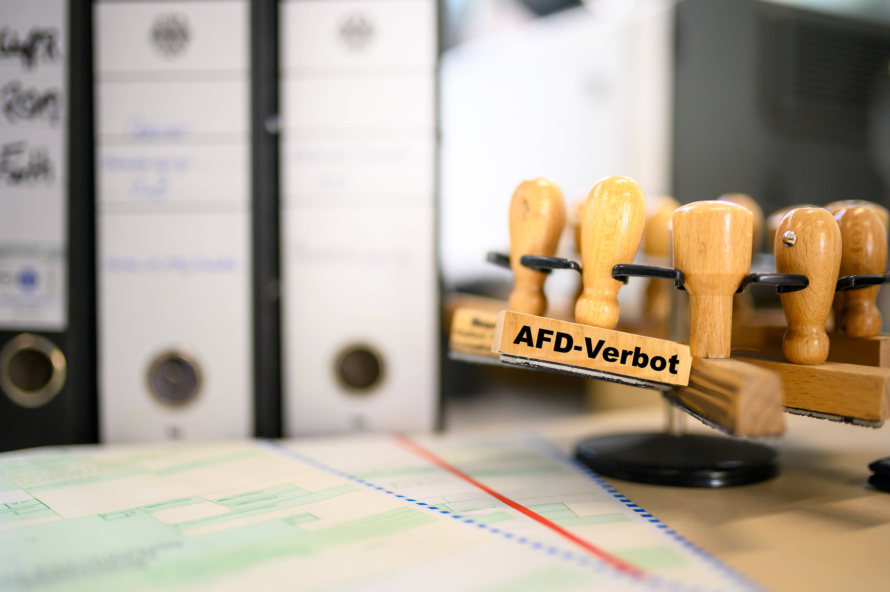 Ein Stempel mit dem Aufdruck: „AfD-Verbot“ hängt zusammen mit anderen Stempeln über einem Schreibtisch.
