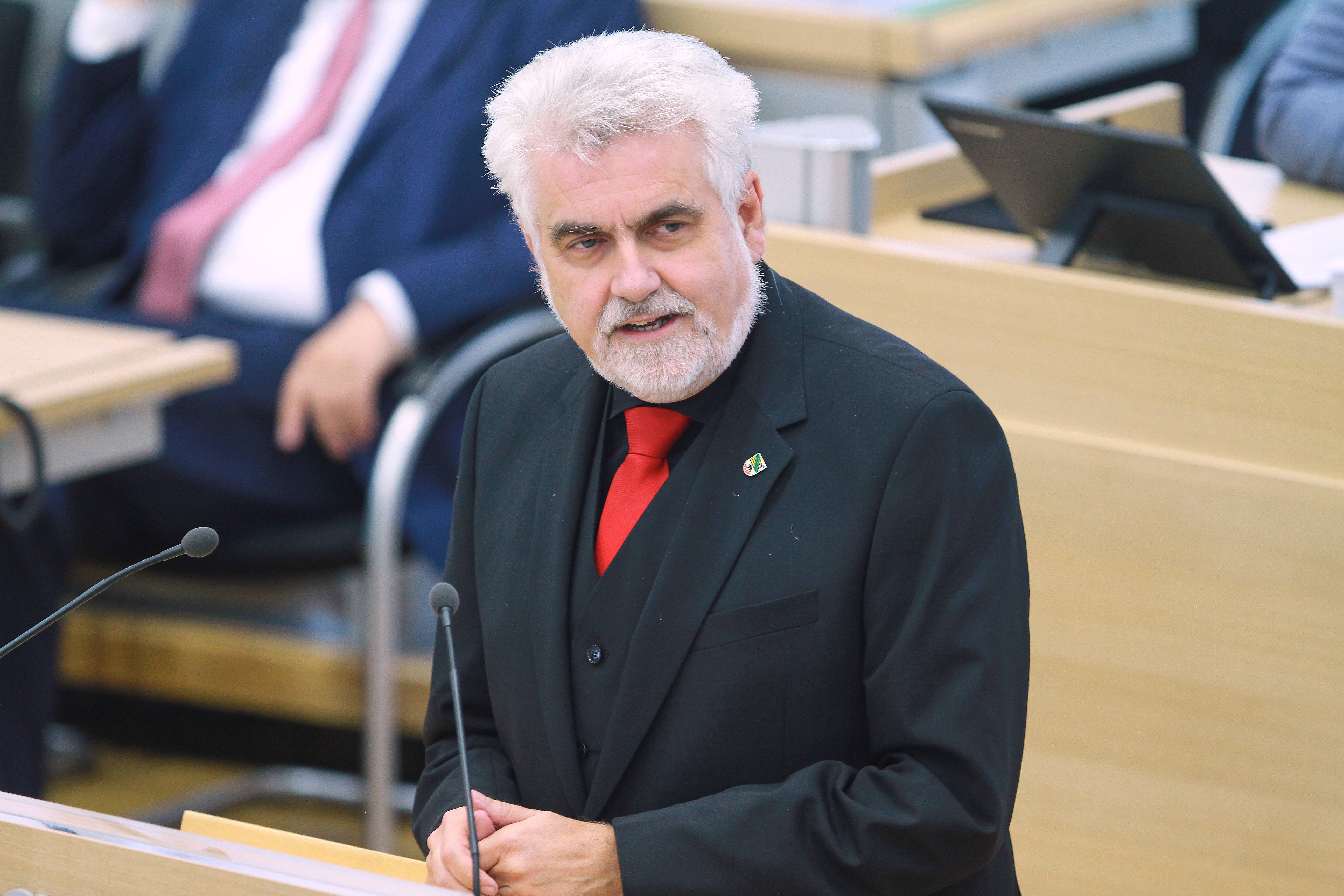 Armin Willingmann steht in schwarzem Anzug mit roter Krawatte vor einem Mikrofon im Landtag von Sachsen-Anhalt