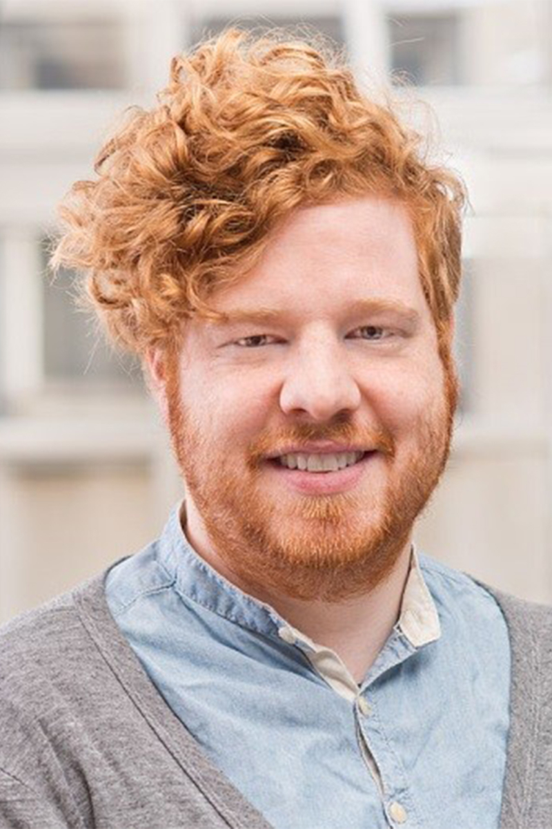 Ein lächelnder Mann mit roten Haaren und Bart.