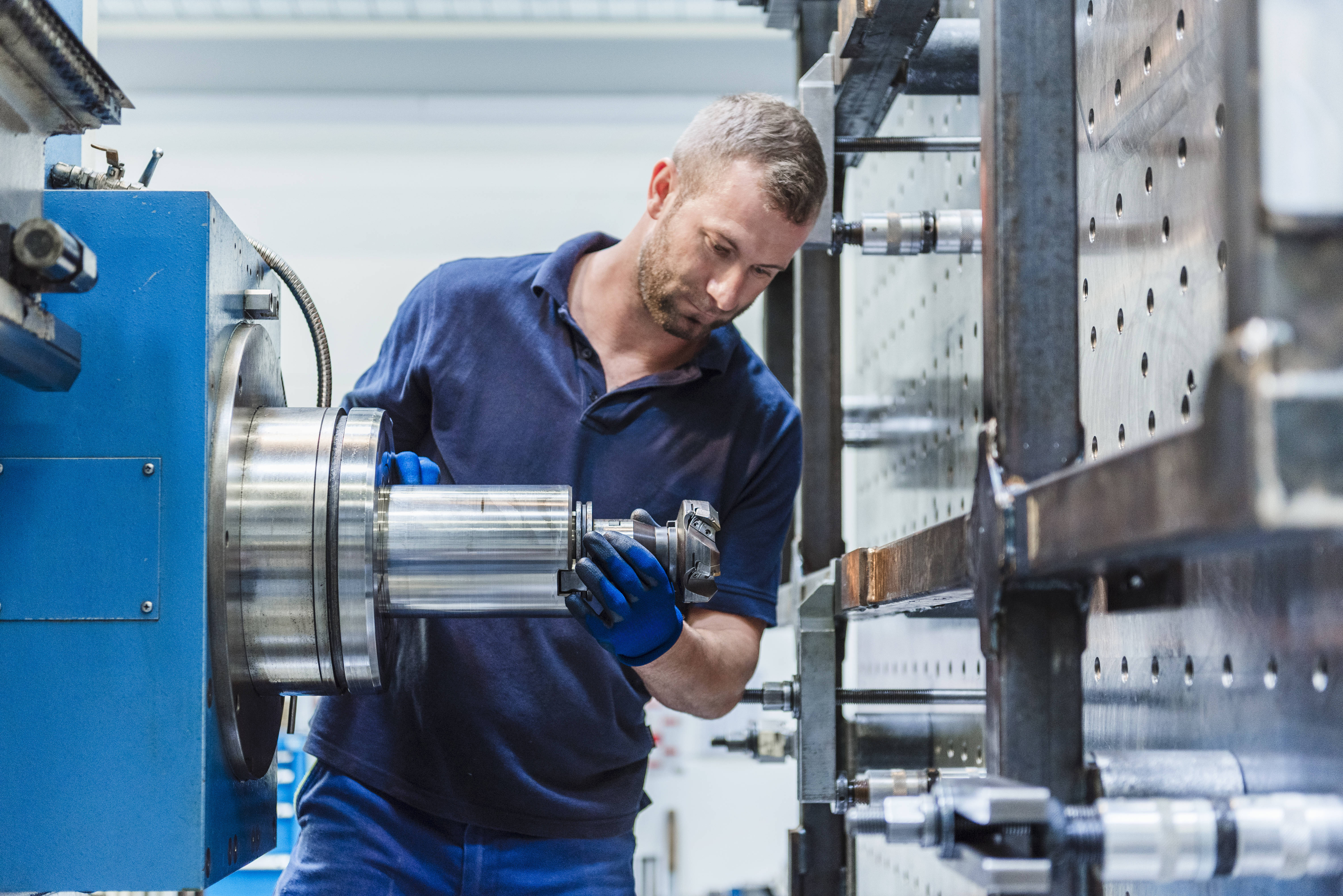 Mann im Arbeitsanzug und -handschuhen an einer Maschine in einer Fabrik