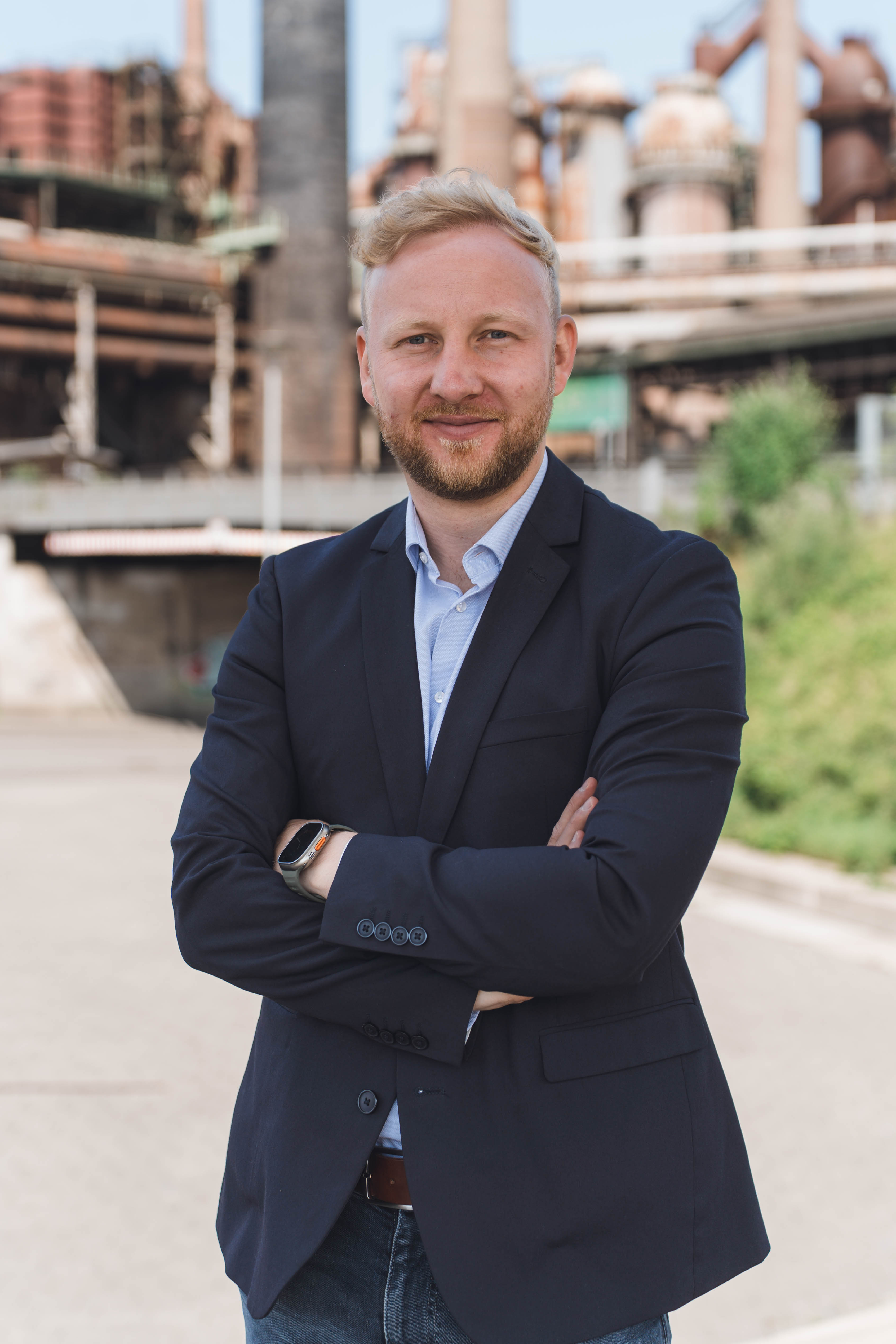Timo Ahr im Anzug vor einer Hochofenanlage
