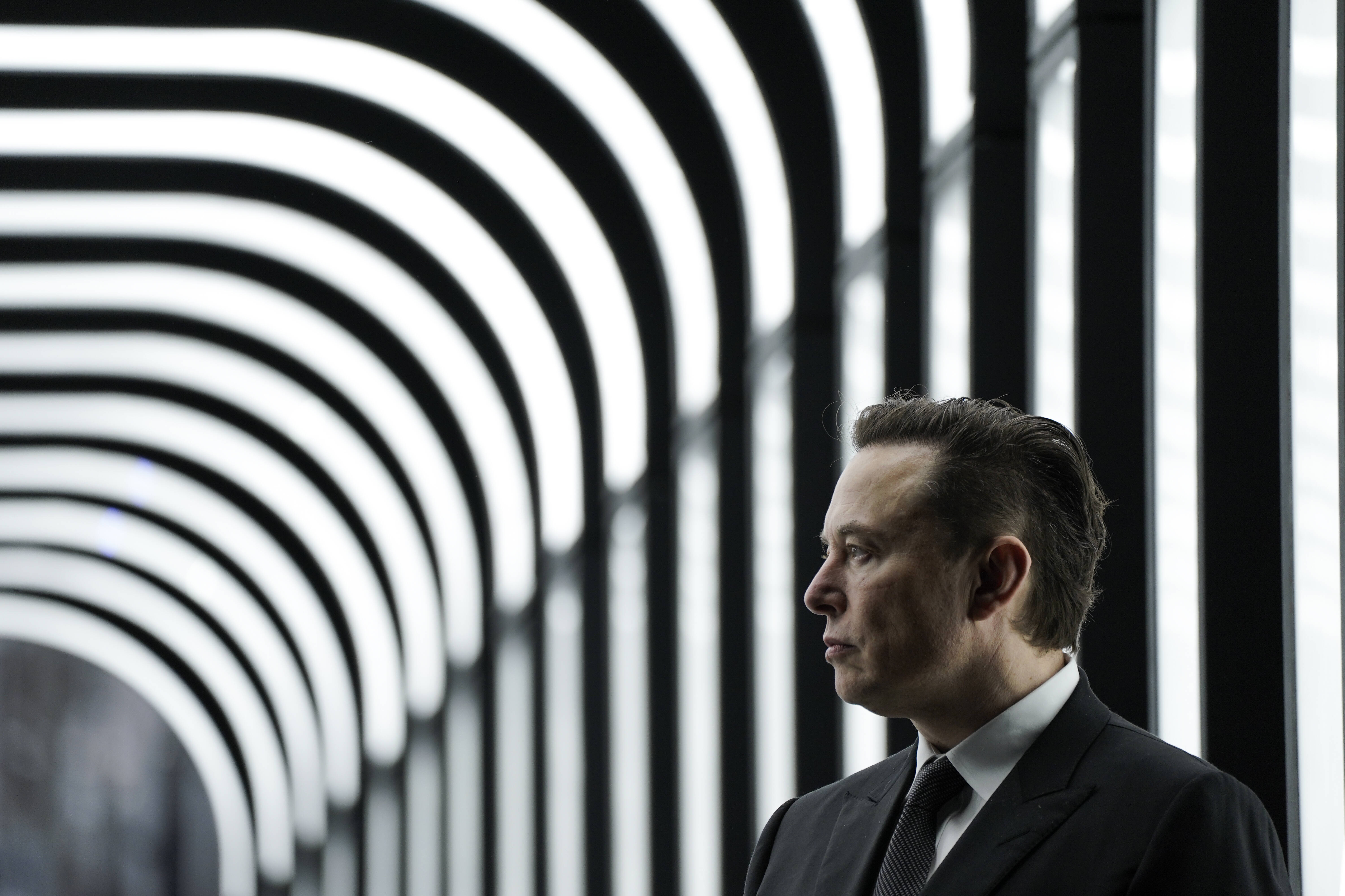 Elon Musk, Seitenaufnahme, vor einem Tunnel mit weißen Leuchtstoffröhren