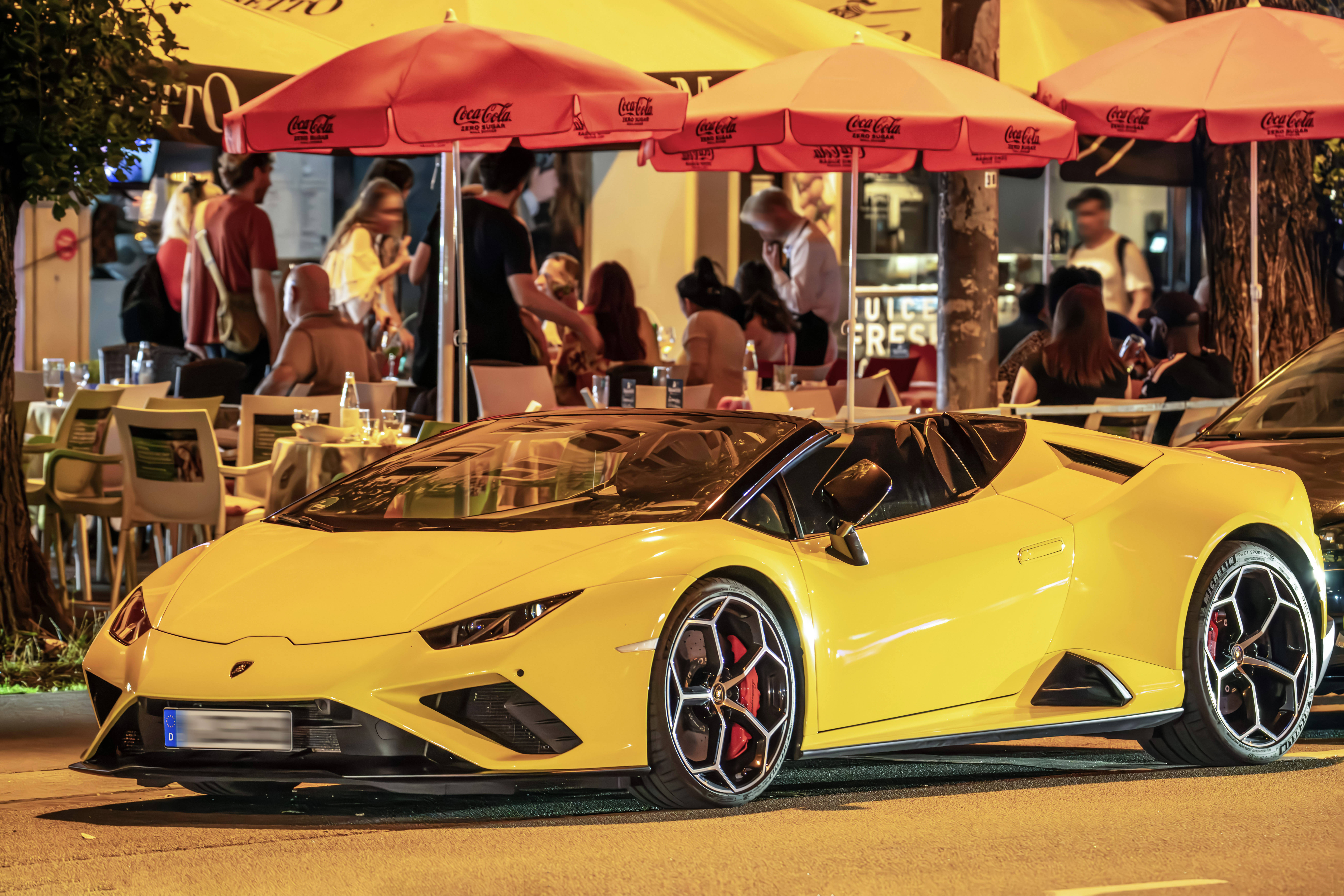 Ein gelber Lamborghini nachts vor einem Cafe mit roten Sonnenschirmen
