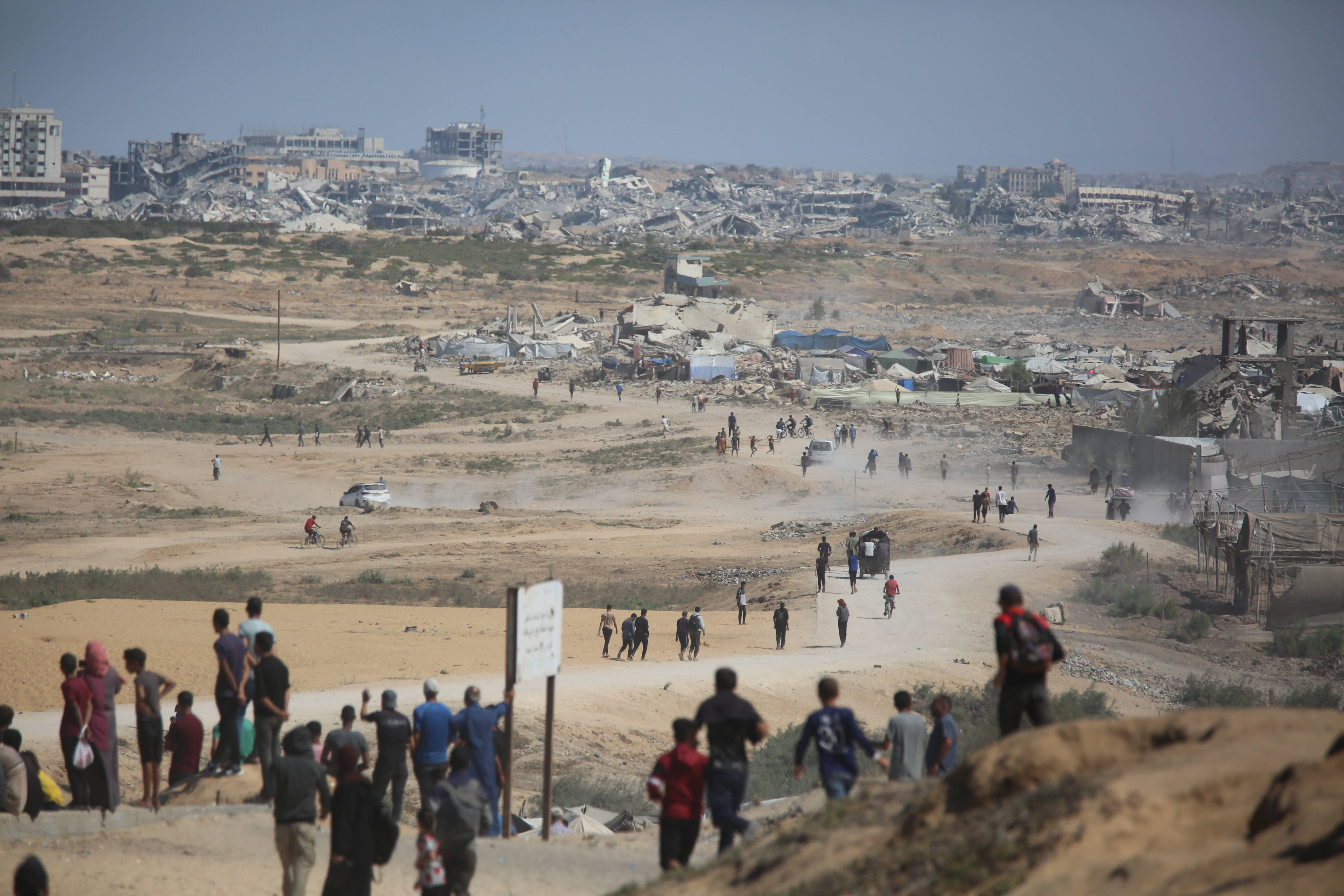 Blick auf das zerstörte Gaza-Stadt, im Vordergrund Menschen, die über eine staubige Straße in die Stadt zurückkehren