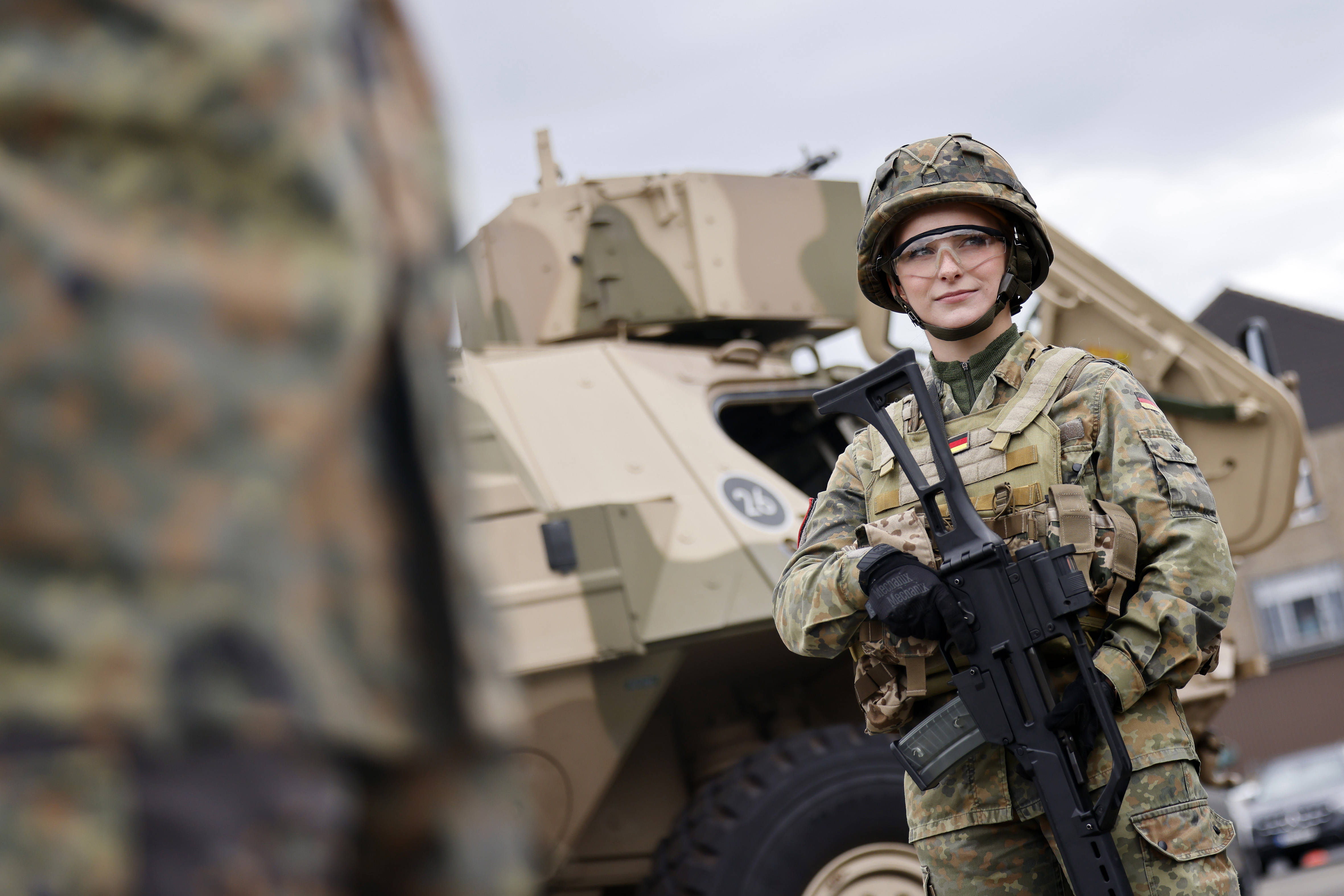 Soldatin im Tarnanzug mit Helm und Gewehr vor einem Panzer