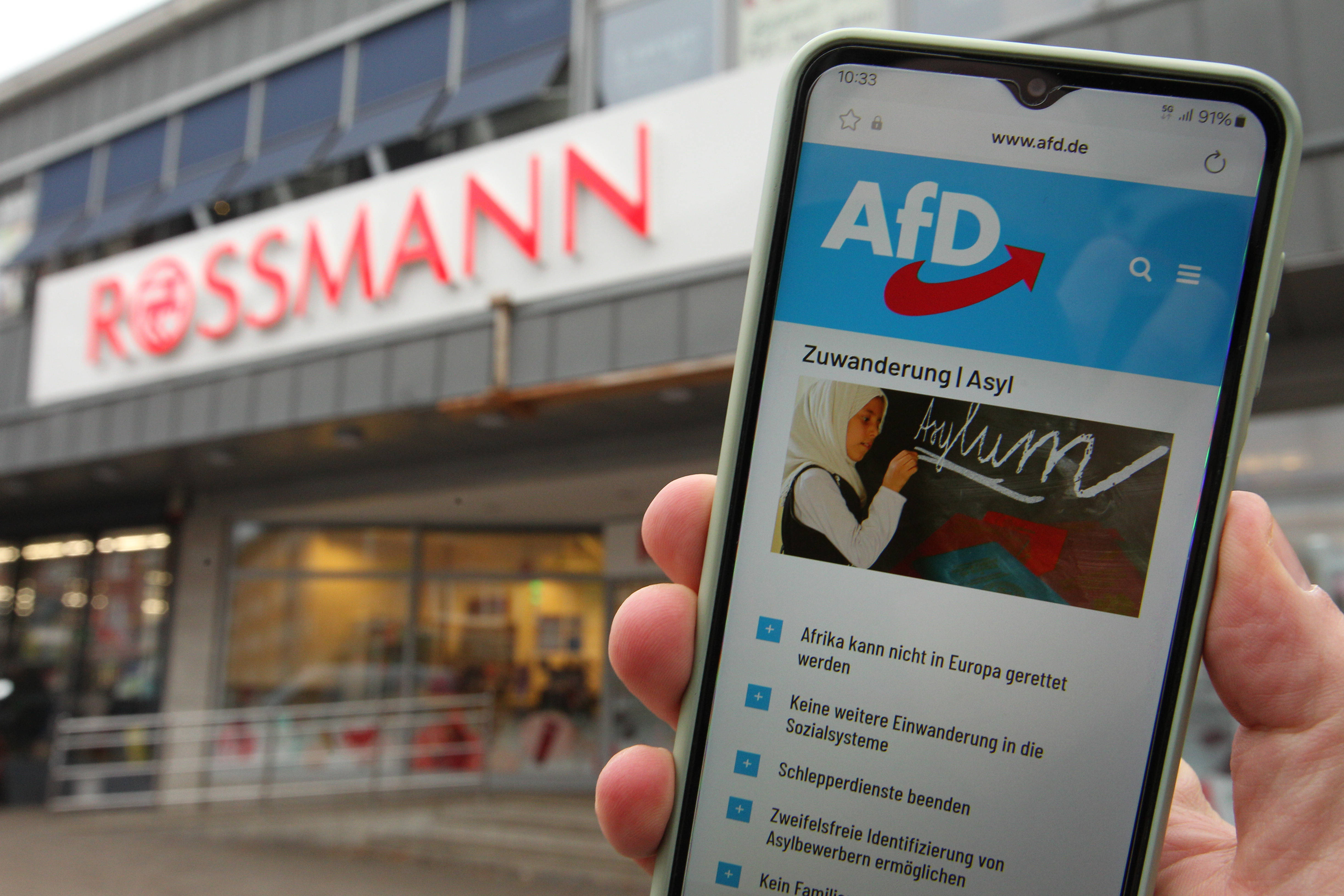 Handy mit der Internetseite der AfD vor einer Rossmann-Filiale