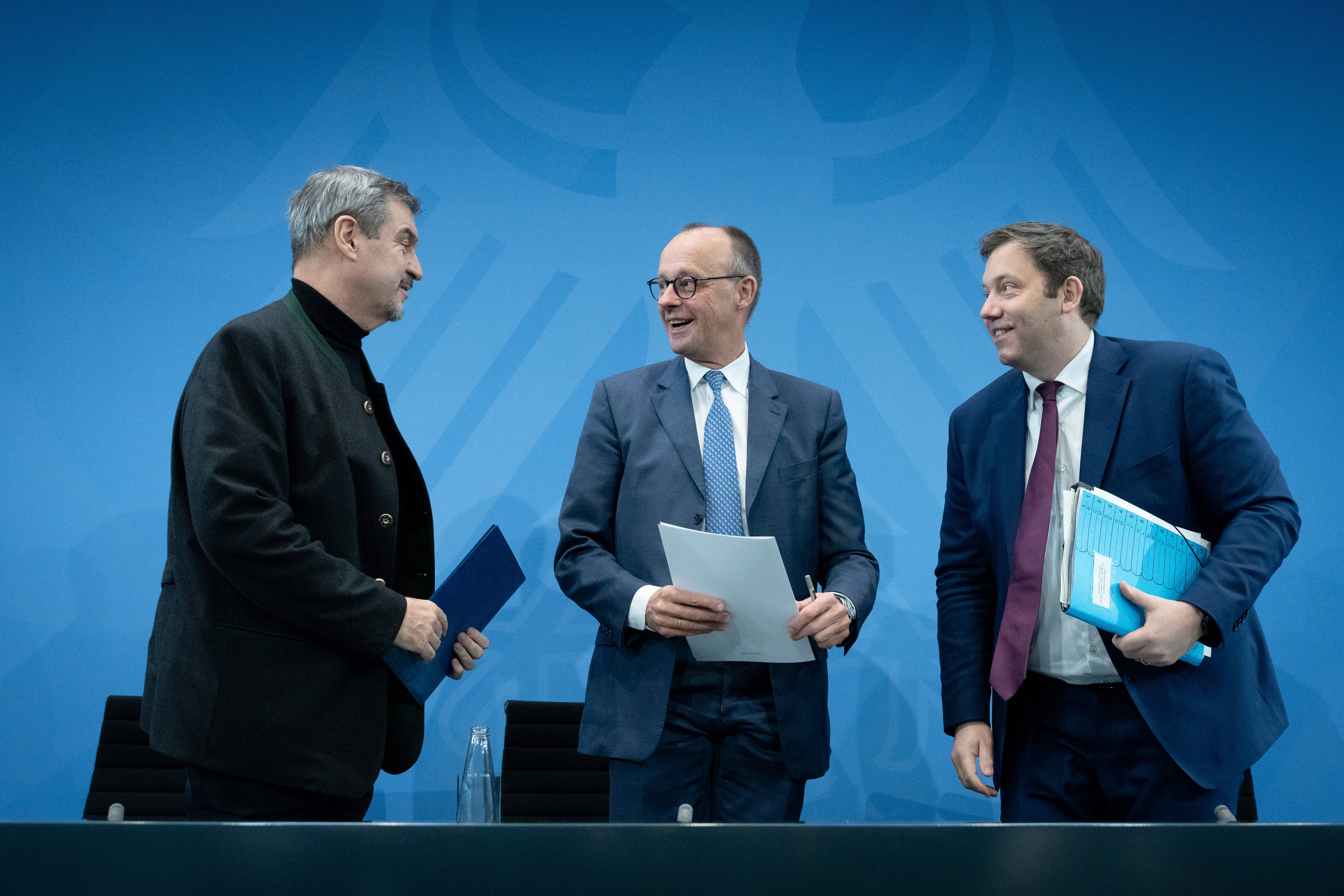 Markus Söder, Friedrich Merz und Lars Klingbeil stehen im Gespräch vor einer blauen Wand mit Bundesadler