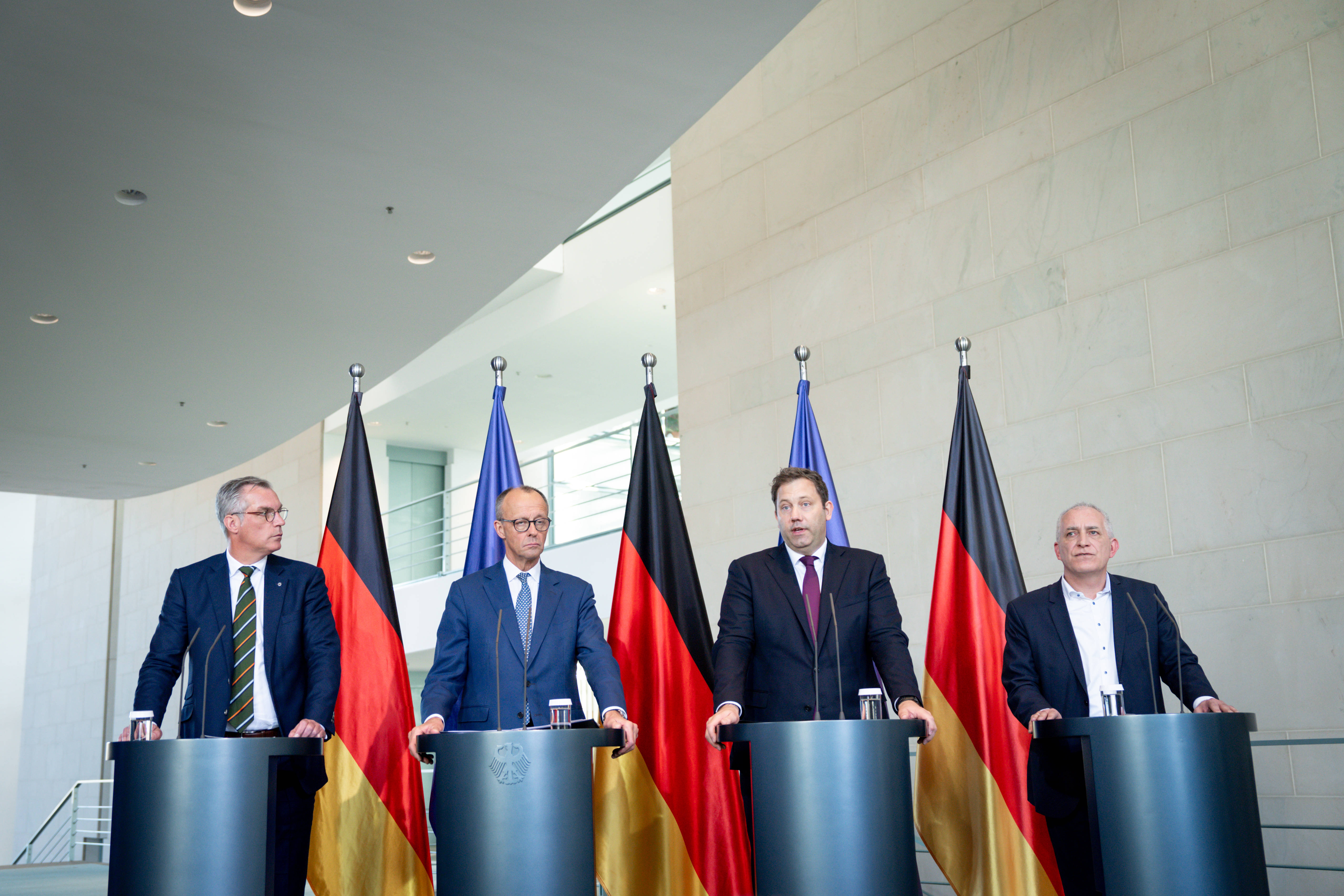 Gunnar Groebler, Friedrich Merz, Lars Klingbeil und Jürgen Kerner an Redepulten vor Deutschland- und Europafahnen