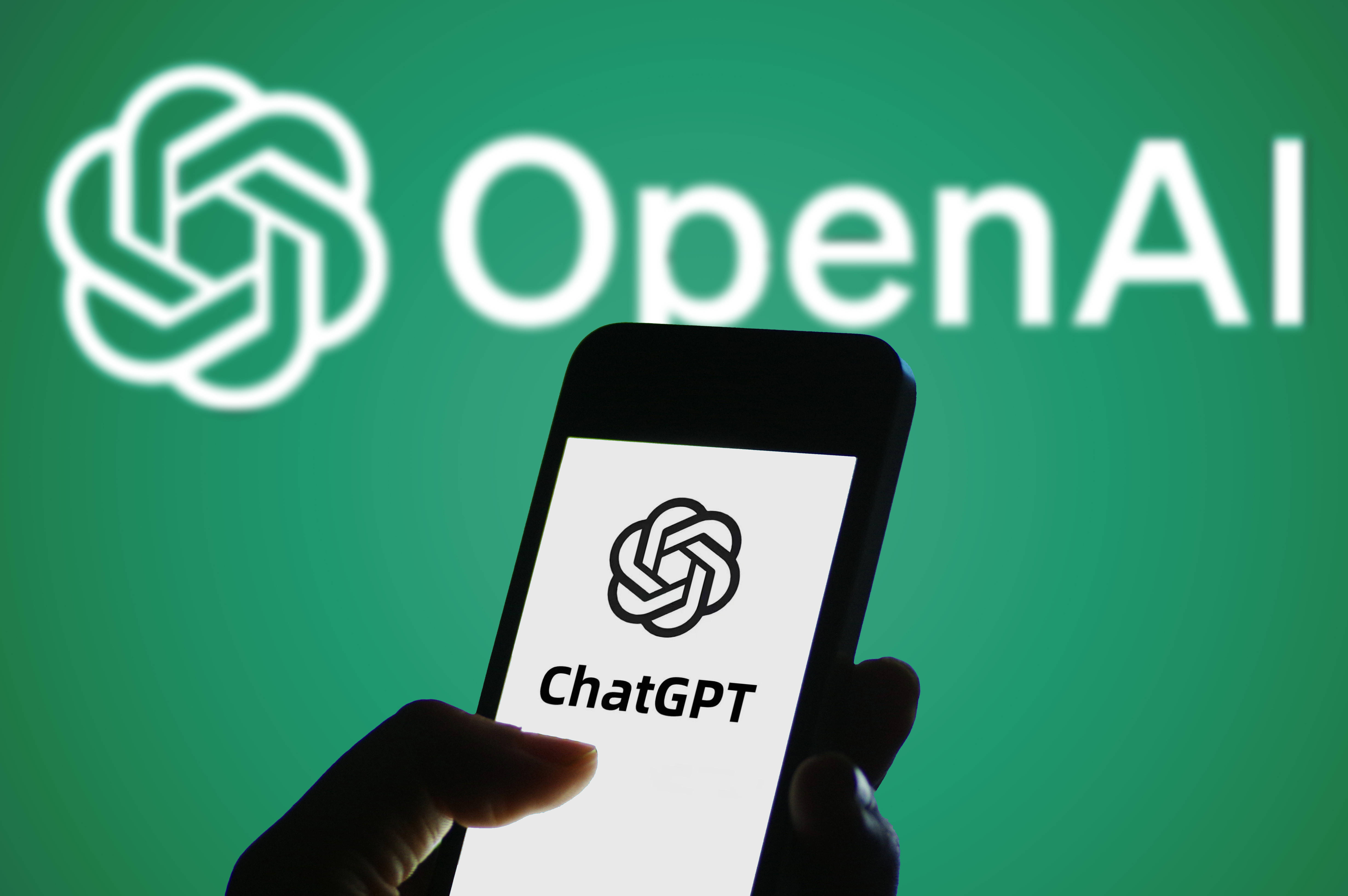 Logo von ChatGPT auf einem Handy vor einem grünen Hintergrund mit dem Logo von "Open AI"