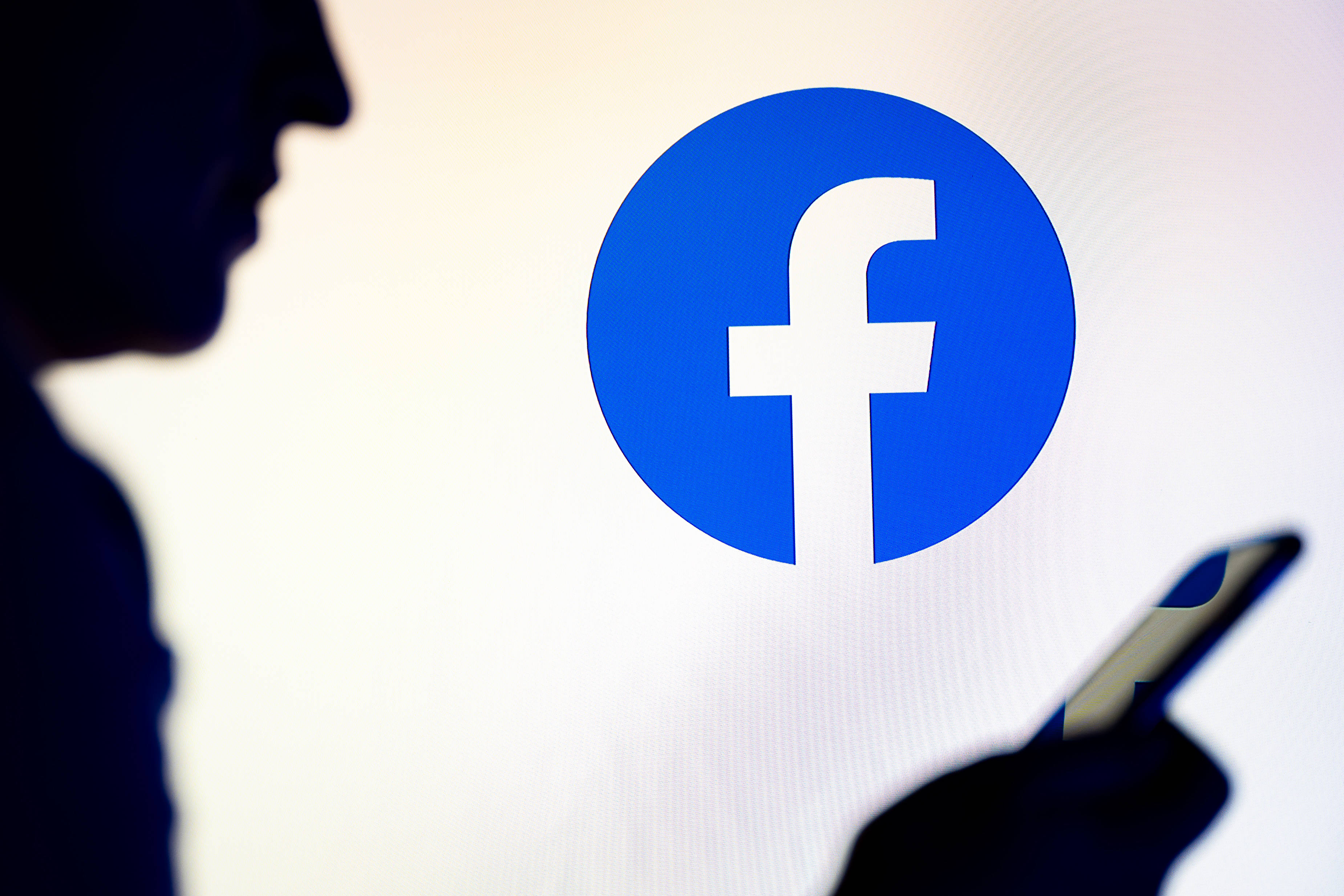 Eine Person ist am Handy, im Hintergrund ist das Facebook-Logo zu sehen.