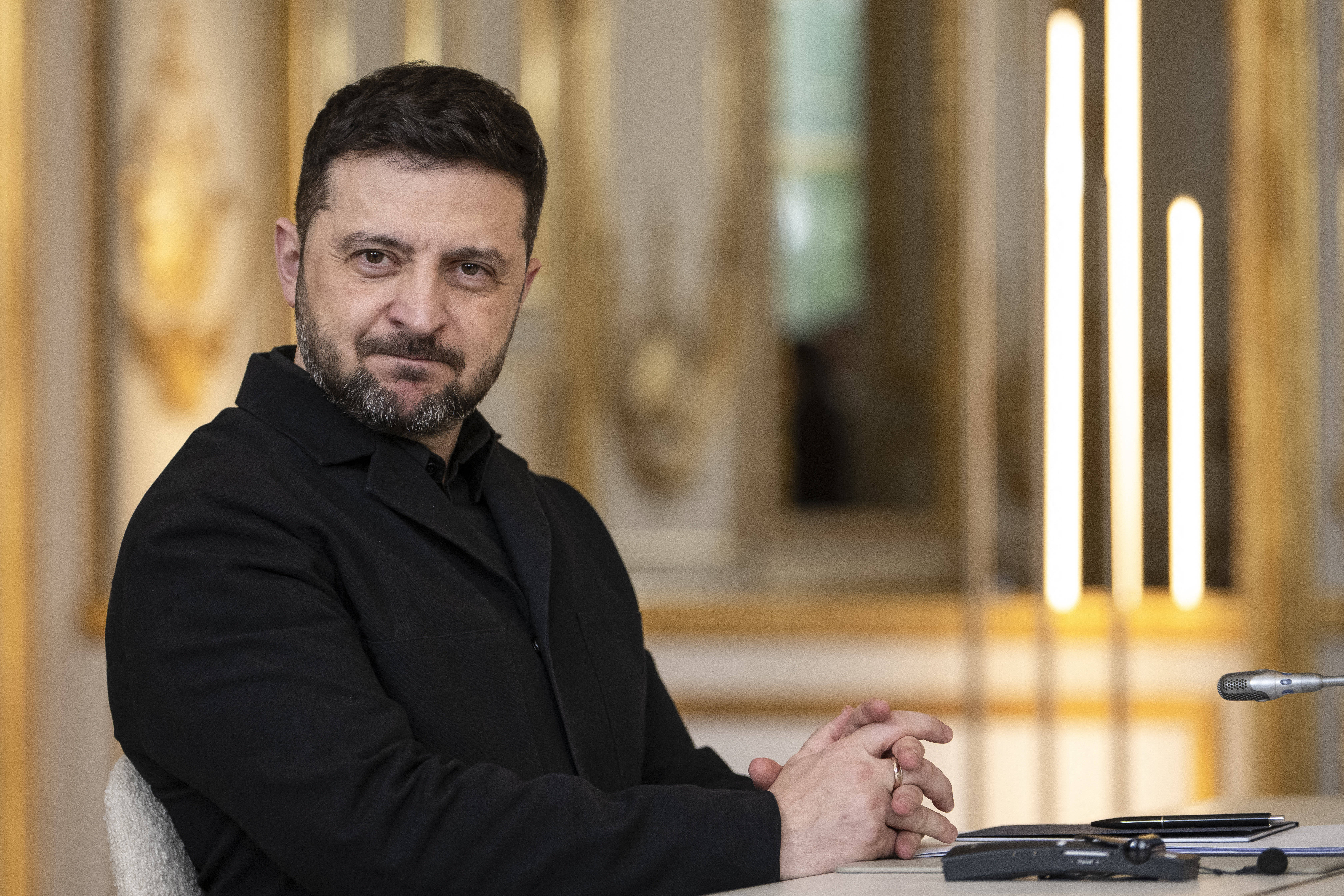 Der ukrainische Präsident Wolodymyr Selenskyj sitzt an einem Tisch und blickt in die Kamera