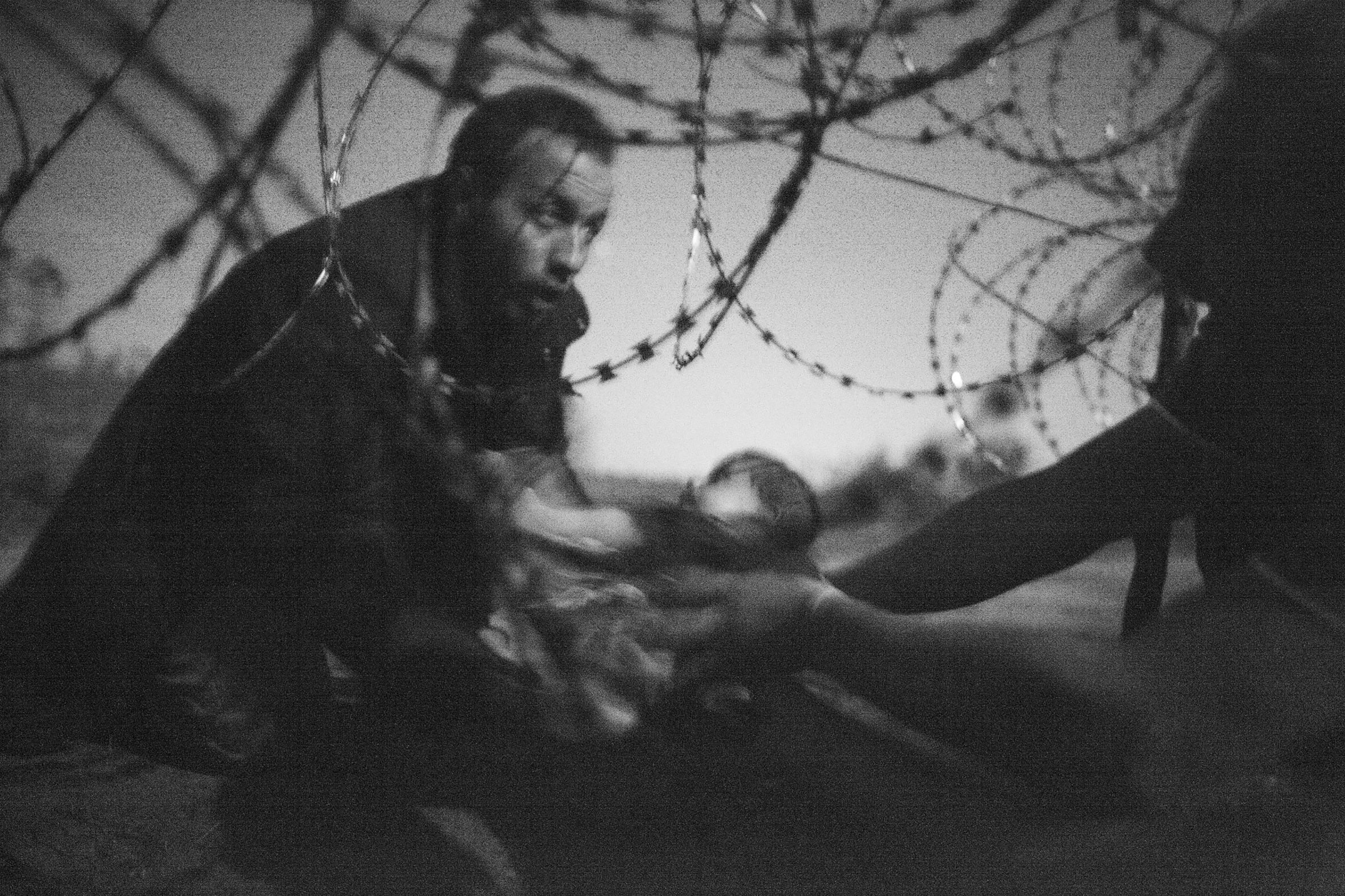 Ein Mann, der ein Baby unter einem Stacheldrahtzaun durchreicht ist das World Press Photo des Jahres 2015