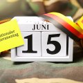 Kalender mit dem Datum 15. Juni und einem gelben Klebezettel mit der Aufschrift "Nationaler Veteranentag" vor Flechtern-Hintergrund und mit schwarz-rot-goldenen Luftschlangen