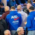 Zwei Männer in blauen Pullovern mit der Aufschrift "AfD-Jugend" in einer Menschenmenge, aufgenommen von hinten