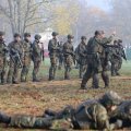 Soldaten im Tarnanzug stehen in einer Herbstlandschaft. Vor ihnen liegen einige mit Gewehren auf dem Bauch.
