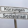 Zwei Wegweiser mit der Aufschrift "Kürzungen" und "Sozialstaat" zeigen in entgegengesetzte Richtungen
