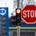 Eine Tafel mit Benzinpreis im Hintergrund, im Vordergrund (unscharf) eine rote Ampel und ein Stopp-Schild