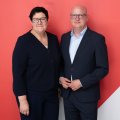 Kathrin Michel und Henning Homann stehen Seite an Seite vor einer roten Wand.